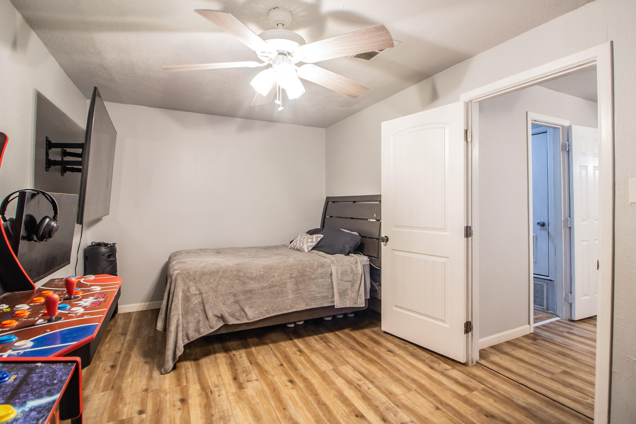 Bedroom with a bed, ceiling fan, wall-mounted television, and arcade game consoles