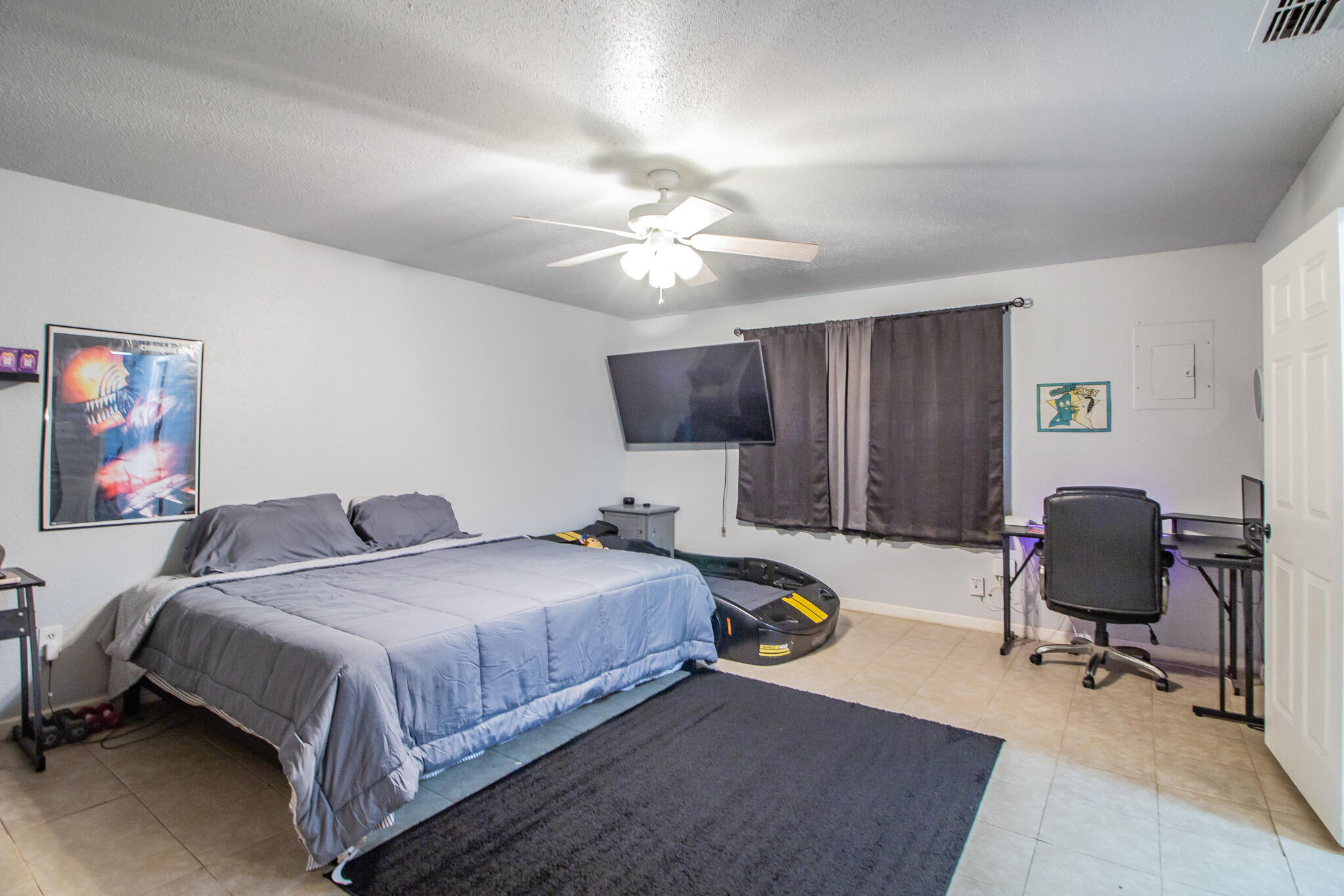 Bedroom with a large bed, wall-mounted television, dark curtains, and desk workspace.