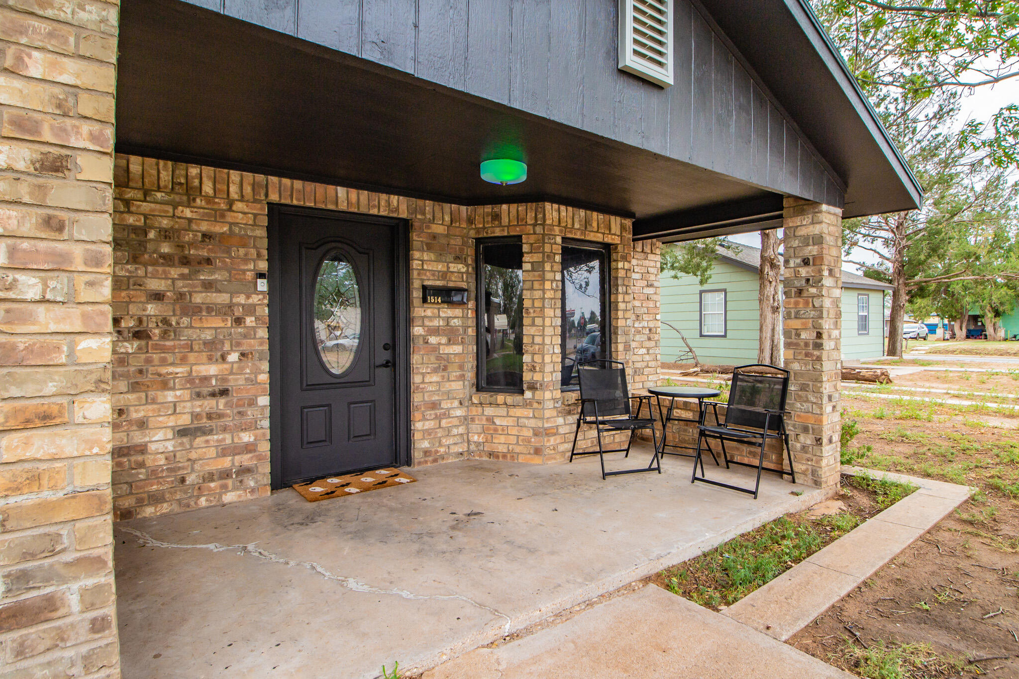 Brick house front porch with a dark entry door and black patio chairs and table.