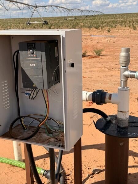 Irrigation control box and pipes in a sandy field beneath a center-pivot system.