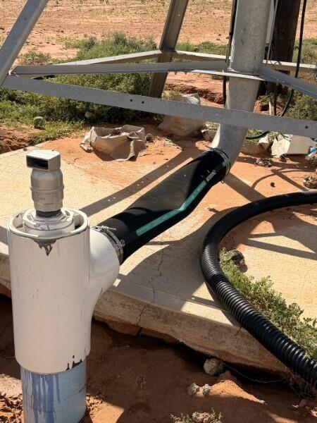 Utility piping and black hoses on sandy ground beneath a metal support structure.