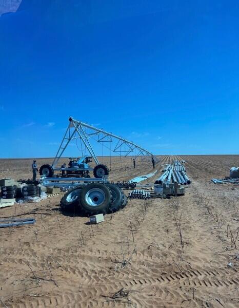Agricultural field with center-pivot irrigation equipment and stacked pipes beneath a clear blue sky.