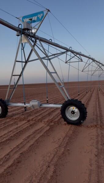 Center-pivot irrigation system over cultivated farmland, with a large support wheel in the foreground.
