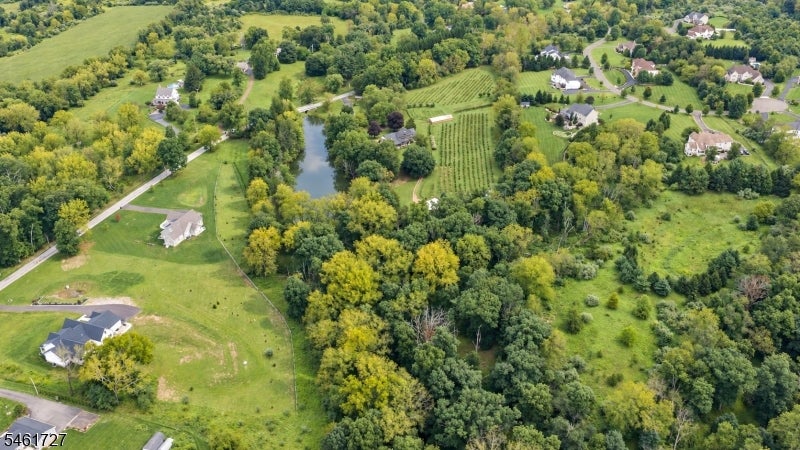 Aerial view of wooded rural property with scattered homes, open fields, a pond, and cultivated rows.