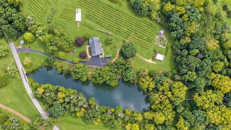 Aerial view of a wooded property with a house, pond, and cultivated garden rows.