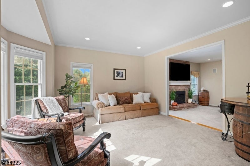Living room with beige sofa, patterned armchairs, large windows, and an adjoining fireplace room.