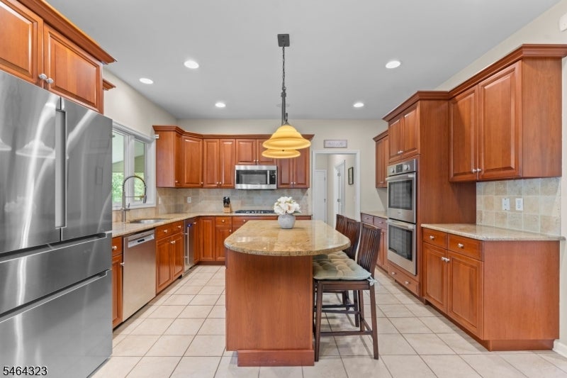 Kitchen with cherry cabinetry, granite island, stainless steel appliances, and tile backsplash.