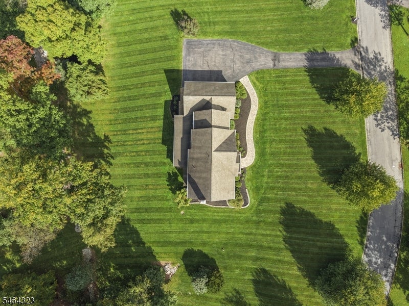 Aerial view of a house surrounded by a broad striped lawn, mature trees, and a paved driveway.