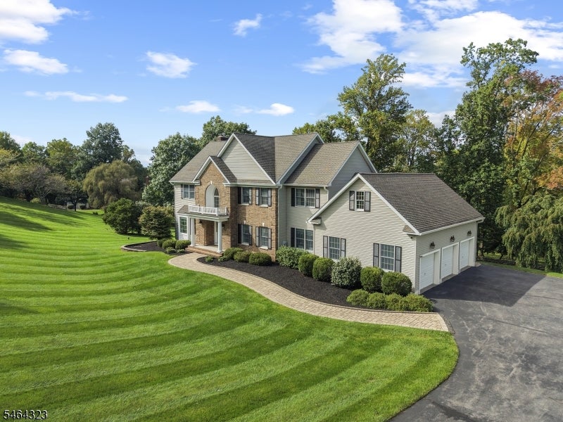 Two-story brick and siding home with an attached garage, curved driveway, and broad striped lawn.