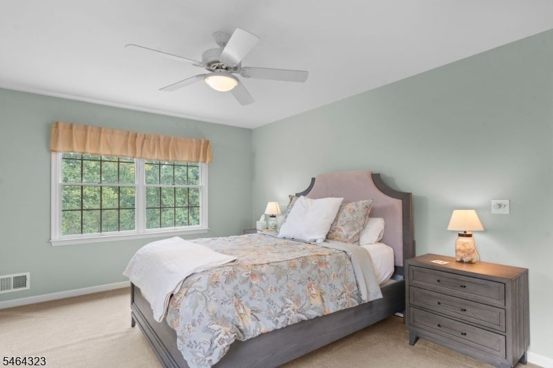 Furnished bedroom with floral bedding, sage-green walls, and a large multi-pane window.