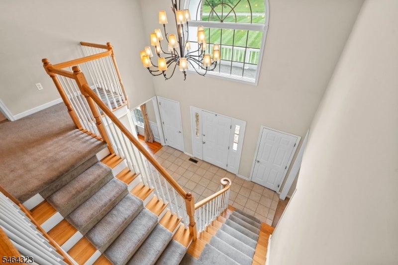 Two-story entry foyer with carpeted stairs, wood railings, a chandelier, and an arched window.