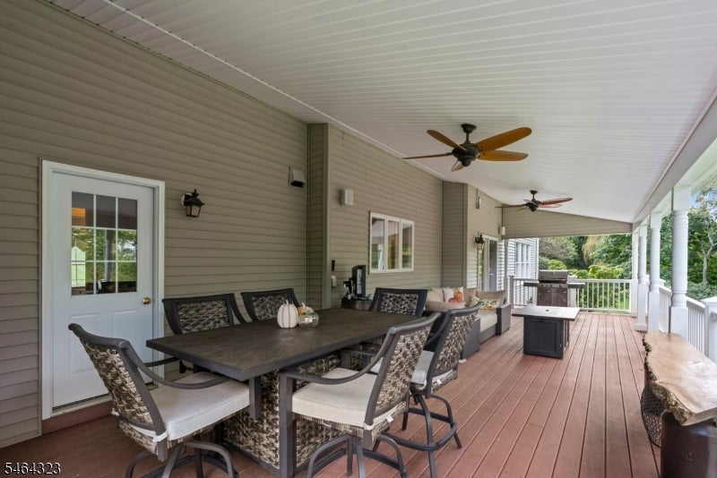 Covered patio with a long dining table, ceiling fans, and trees beyond the railing.