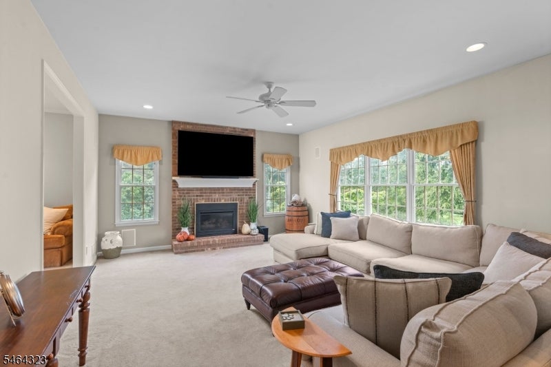 Living room with a brick fireplace, beige sectional, large curtained windows, and ceiling fan.
