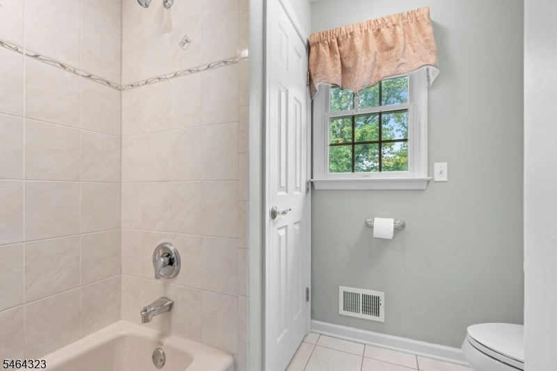 Bathroom with a tiled tub and shower beside a window with a peach valance.