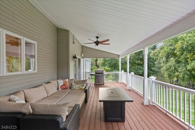 Covered rear deck with outdoor seating, grill, ceiling fan, and wooded surroundings.