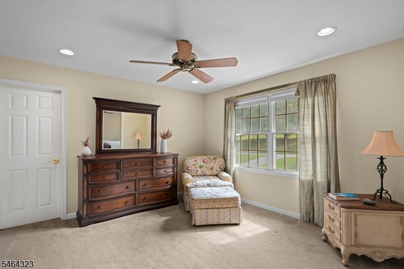 Furnished bedroom with a dark wood dresser, floral chair, and large curtained window.