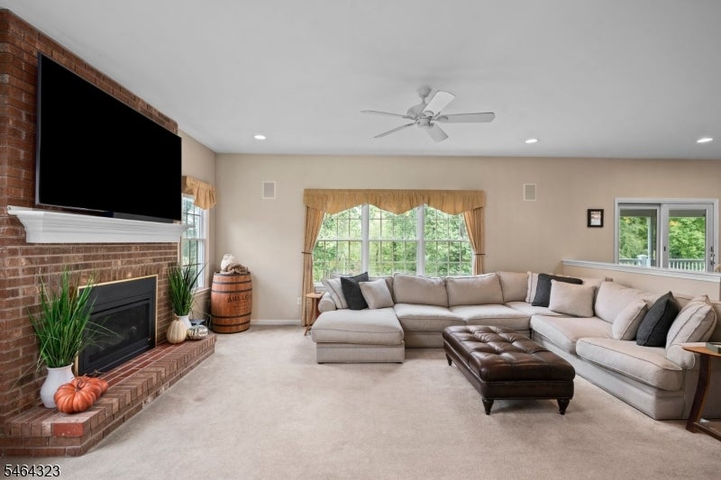 Living room with a brick fireplace, television, sectional sofa, and large windows overlooking greenery.