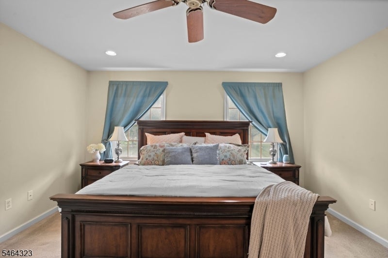 Staged bedroom with a dark wood bed between windows with blue curtains and matching nightstands.