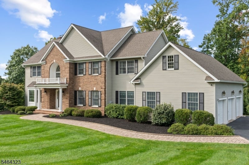 Two-story home with brick entry, pale siding, landscaped lawn, and an attached garage.
