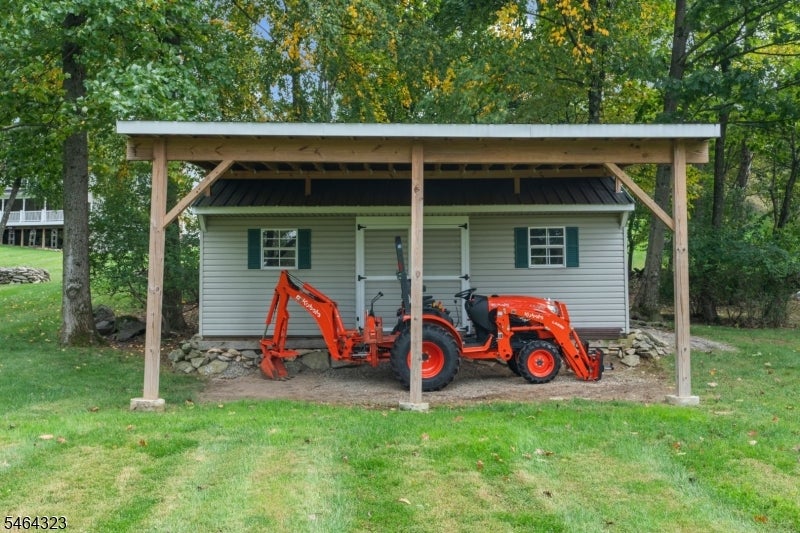 Outbuilding under a timber shelter with an orange compact tractor parked inside.