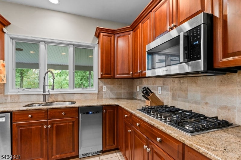 Kitchen with reddish-brown wood cabinets, granite counters, and a gas cooktop beneath a stainless microwave.