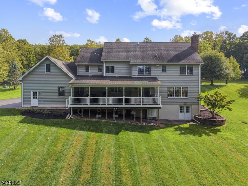 Rear of a large gray house with a raised covered deck and broad green lawn.