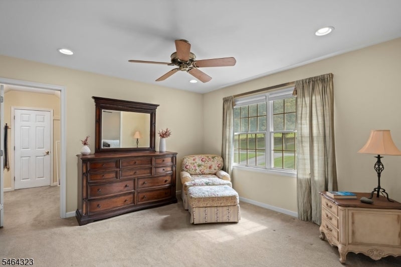 Furnished room with a dark wood dresser, floral chair and ottoman, and a curtained window.