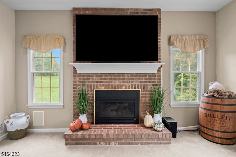 Living room with a brick fireplace, television above the mantel, flanking windows, and fall decorations.