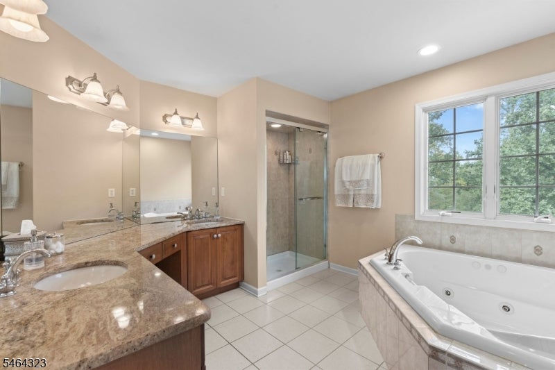 Bathroom with a corner whirlpool tub, glass-enclosed shower, and granite double-sink vanity.