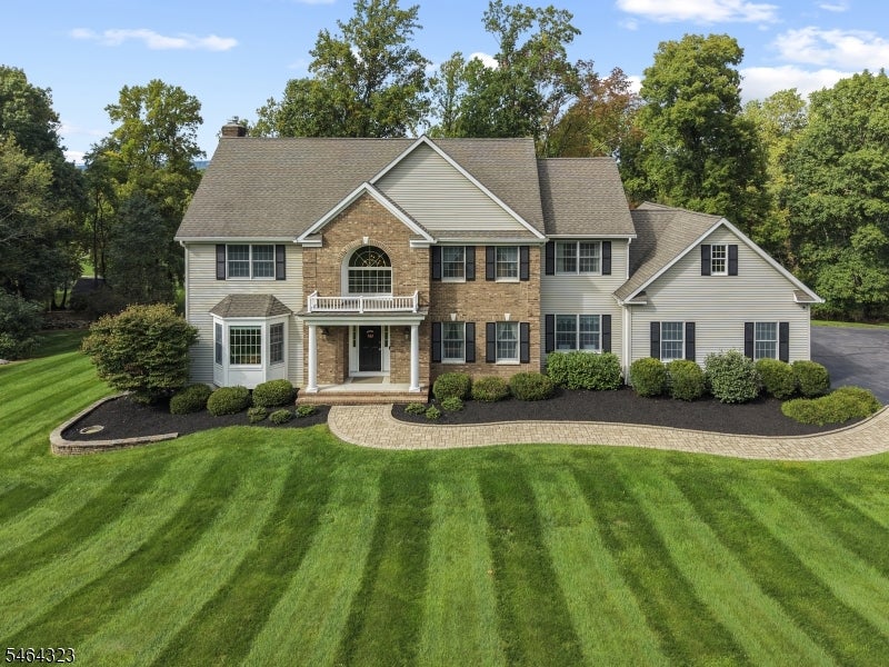 Two-story stone and gray-sided home with a small balcony, curved walkway, and striped lawn.