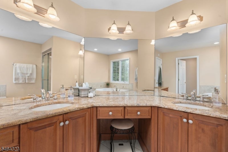 Bathroom vanity with double sinks, granite counters, mirrored walls, and a stool beneath the center counter.