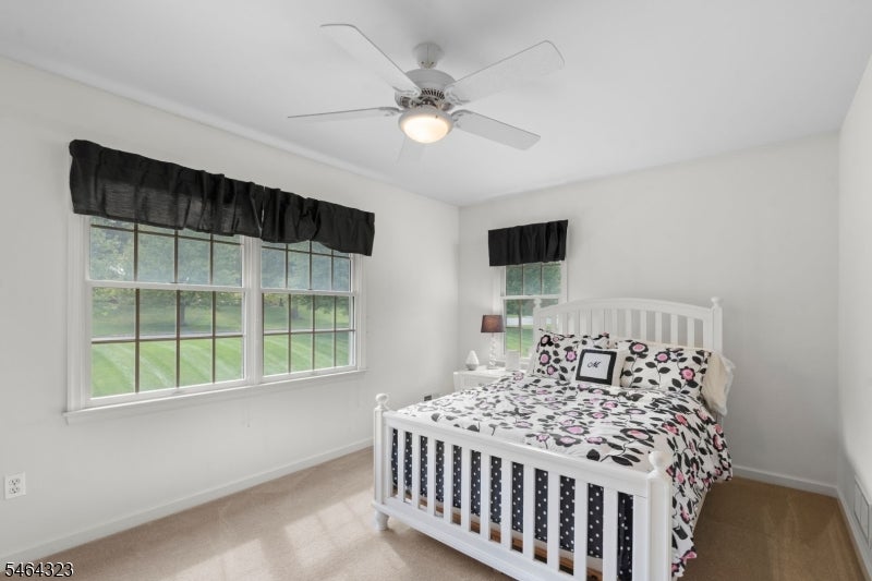 Bedroom with a white bed in floral bedding, ceiling fan, and windows overlooking a lawn.