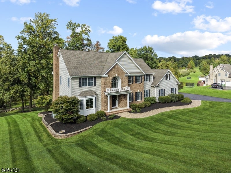 Two-story brick and gray-sided home with a white balcony, landscaped beds, and a broad striped lawn.