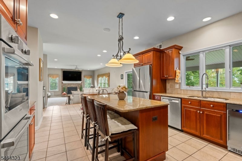 Kitchen with a granite island, reddish wood cabinets, stainless steel appliances, and an open view into the living area.