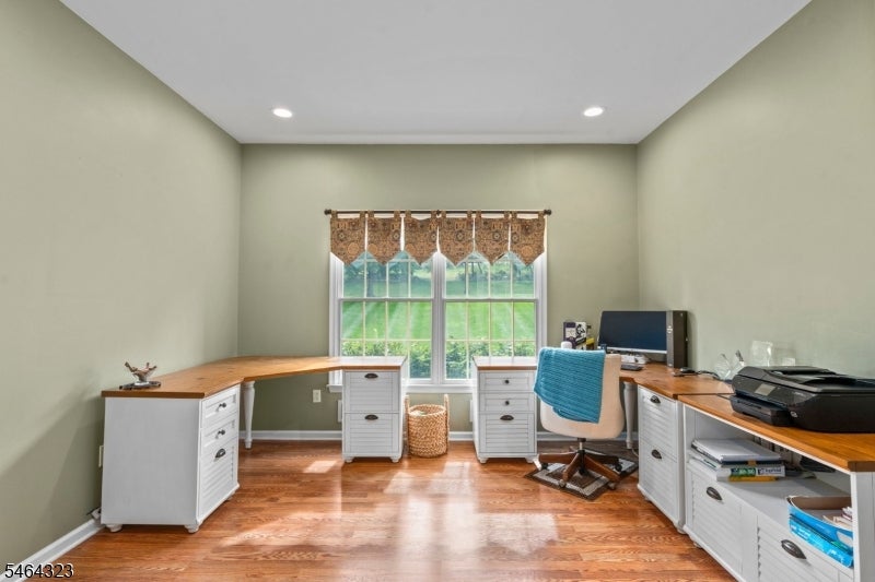 Home office with wraparound wood countertops, white cabinetry, and a window overlooking greenery.