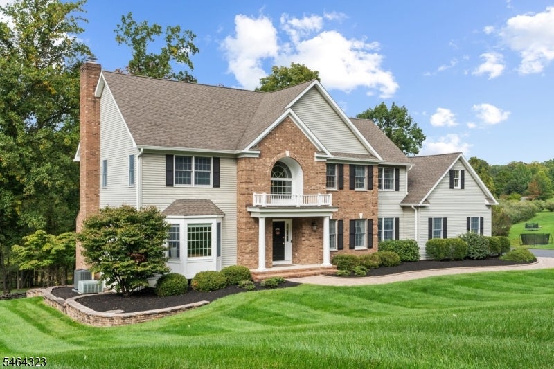 Two-story brick-and-siding home with an arched entry, manicured lawn, and landscaped front beds.