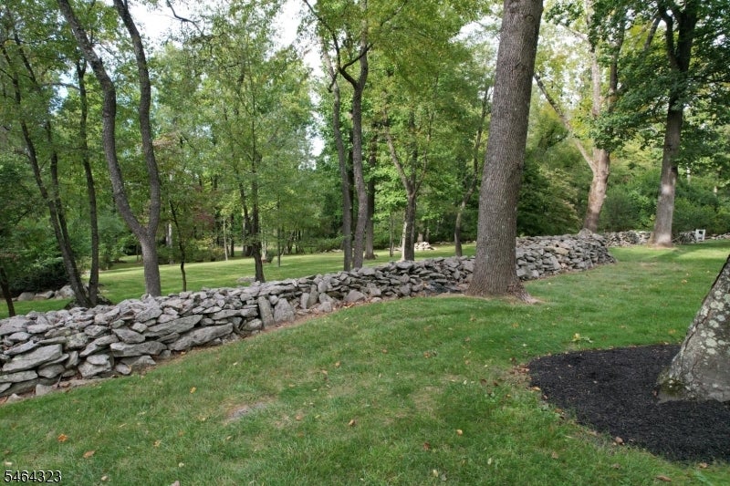 Landscaped yard with a dry-stone wall, mature trees, and a broad green lawn.