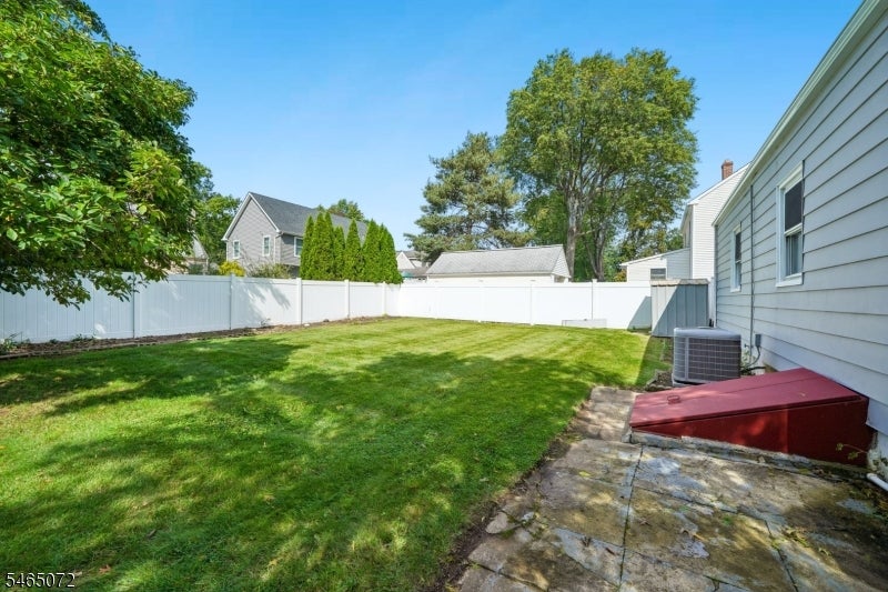 Fenced backyard with a broad lawn, mature trees, and a stone patio beside the house.