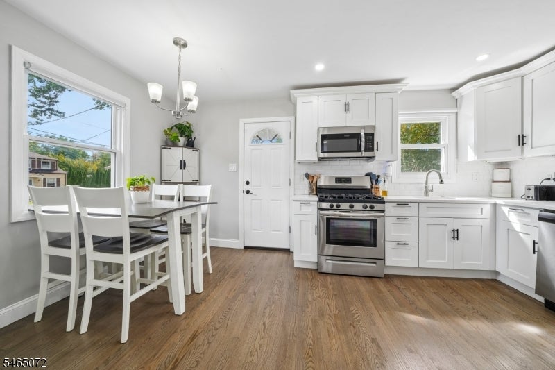 Kitchen with white cabinets, stainless steel appliances, and a dining table beside a large window.