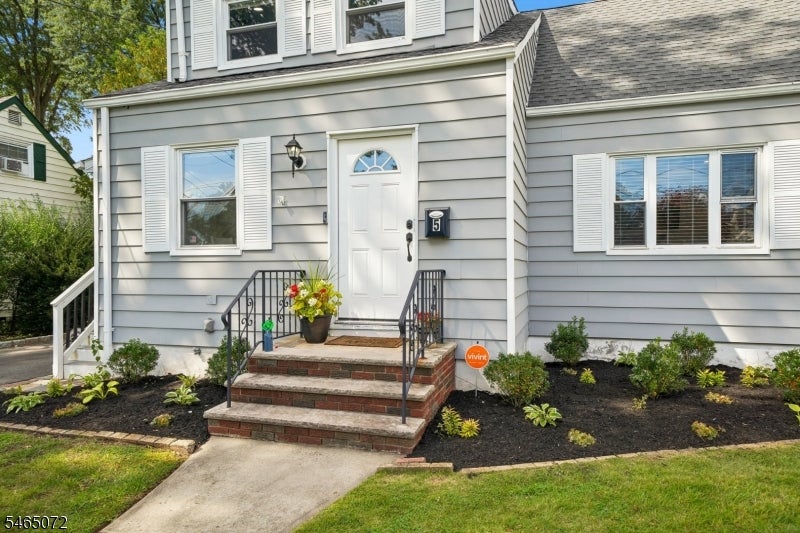 Gray-sided house front with white entry door, brick steps, black railings, and landscaped beds.