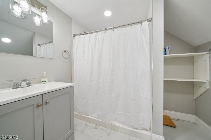 Bathroom with gray vanity, white shower curtain, built-in shelves, and marble-look tile floor.