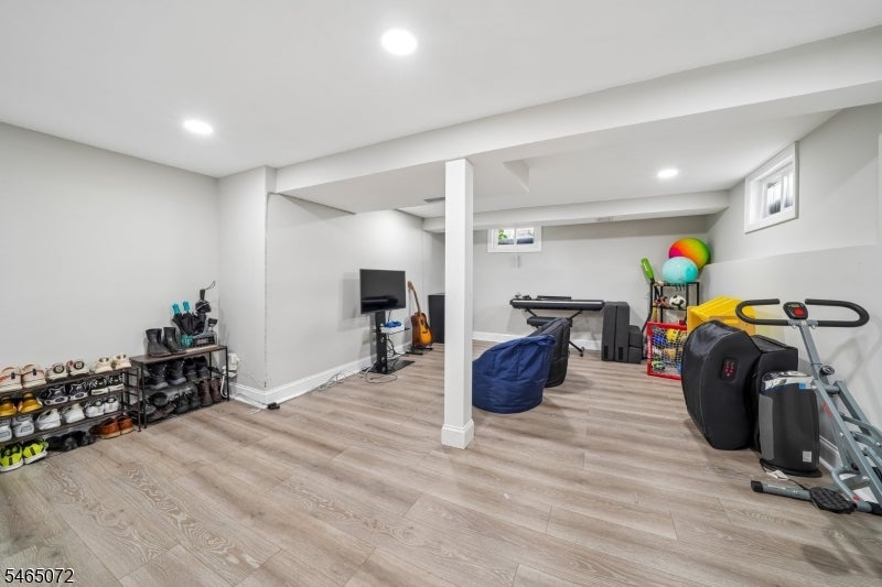 Finished basement recreation room with light wood-look flooring, exercise equipment, and a television.