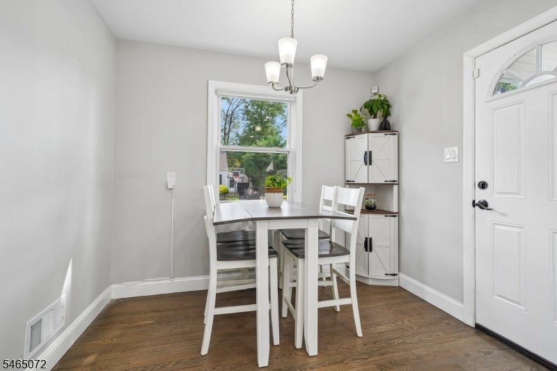 Dining area with a white table, corner cabinet, wood flooring, and garden-facing window beside the front door.