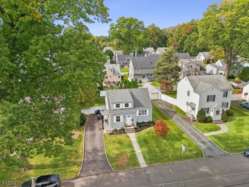 Aerial view of a gray-sided home with a front lawn, driveway, and mature trees.