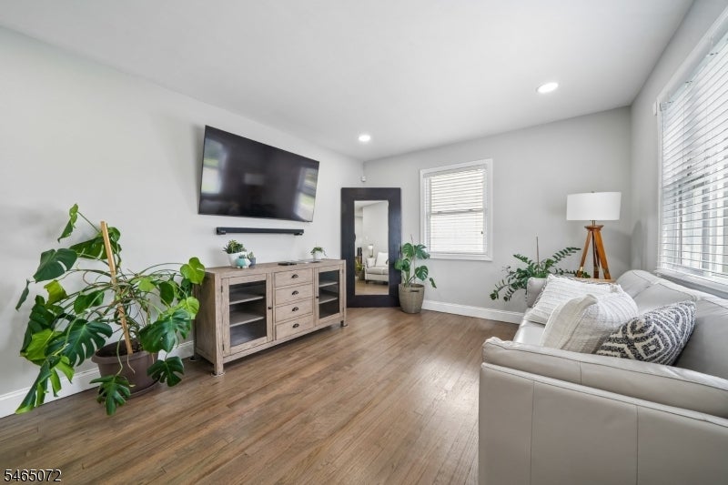 Furnished living room with wood floors, a white sofa, leafy plants, and a wall-mounted television.