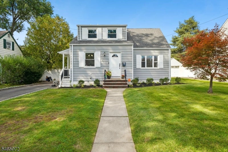 Gray-sided house with a large upper dormer, front steps, and a walkway across the lawn.