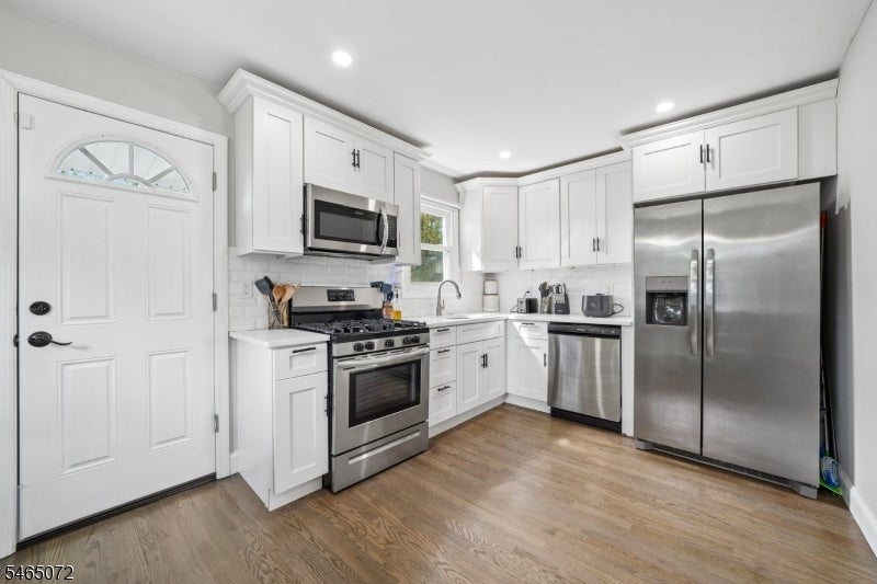 Kitchen with white cabinets, stainless steel appliances, and light wood flooring.