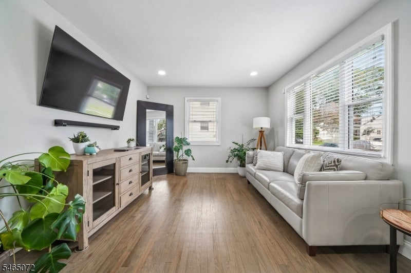 Living room with a white sectional sofa, large windows, wood floors, and a wall-mounted TV.