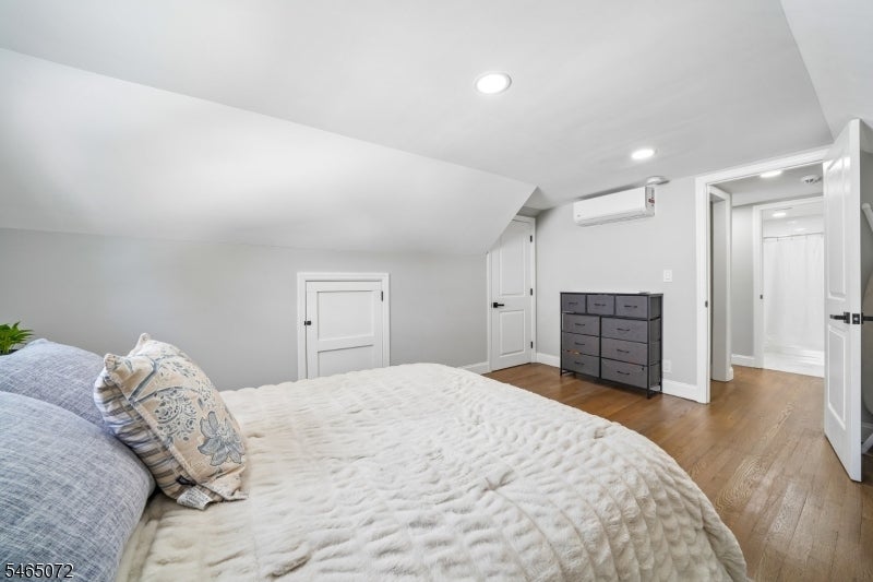 Attic bedroom with a white-quilted bed, sloped ceiling, dark dresser, and open bathroom doorway.