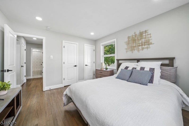 Furnished bedroom with a large white bed, gray accent pillows, hardwood floors, and a bathroom doorway.